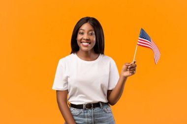 Yurtdışında eğitim, Amerika 'da eğitim, göç kavramı. Portakal rengi arka planda Amerikan bayrağı taşıyan genç, pozitif siyah bir kız öğrenci.