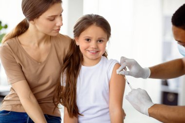 Annesiyle birlikte doktoru ziyaret eden tatlı, mutlu bir kız. Hastanede kovid 19 aşısı yaptırıyor. Ebeveynler ve çocuklar klinikte koronavirüse karşı aşı oluyorlar. Viral hastalıklara karşı koruma