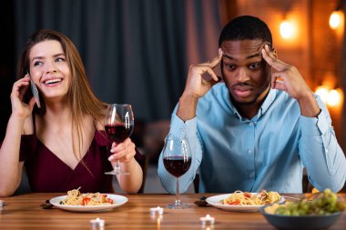 Sıkıcı adam, sarhoş sevgilisinin yanında oturmuş cep telefonuyla konuşuyor. Sinirli Afrikalı Amerikalı Adam Şakaklara Dokunuyor, Üzgün ve Yalnız Hissediyor. Irklar Arası Sorunlar Konsepti, Boş Alan