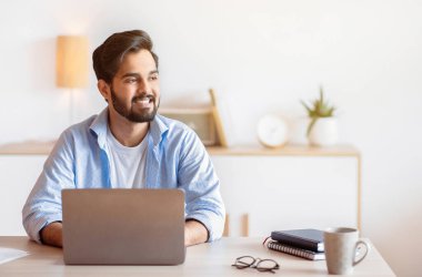 İçişleri Bakanlığı 'nda dizüstü bilgisayarla oturmuş mutlu bir ifadeyle yüzünü çeviren dalgın bir Arap' ın portresi. Gülümseyen Doğulu Serbest Çalışan Adam Başarılı İş Stratejisi Düşünüyor, Boşluğu Kopyala