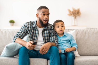 Sorgulanabilir televizyon içeriği. Siyah Baba ve Oğul 'un televizyon izlemesi, babanın evde koltukta oturan uygunsuz film sahnesiyle kanalı değiştirmesi. TV Programı ve Ebeveyn Kontrolü