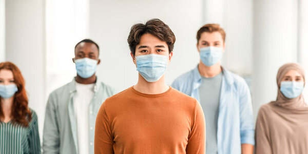 New Reality, Epidemic Concept. Portrait of asian male teen wearing protective medical mask standing with diverse group of international people in the blurred background, posing and looking at camera