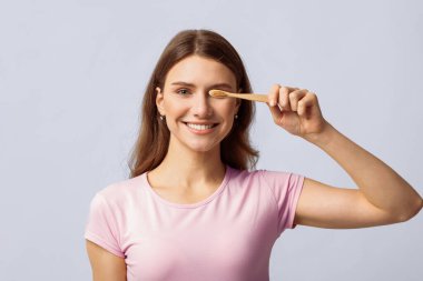 Uzun saçlı bir kadın bambu bir diş fırçasını arka planda tutarken gülümsüyor, sürdürülebilir yaşam ve çevre dostu uygulamalara bağlılığını gösteriyor.