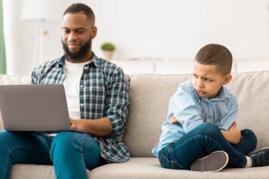 Kayıtsız Kara Baba, Oğlu 'nu ihmal ediyor, dizüstü bilgisayar kullanıyor ve evdeki koltukta oturan küçük çocuğu gücendirmiyor. Kötü aile ilişkisi sorunu, gönülsüz baba ve mutsuz çocuğu.