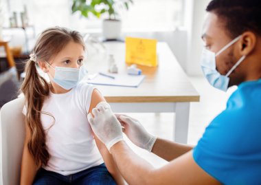 Erkek doktor ya da hemşire klinikteki küçük hastalara koronavirüs aşısı yapıyor. Güzel bir kız covid-19 'a karşı bağışıklık kazanıyor. Tıbbi hizmet ve viral hastalık önleme kavramı