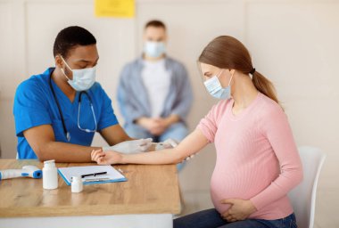 Afro-Amerikalı doktor Covid-19 aşısını sağlık merkezindeki genç hamile kadına enjekte ediyor. Muhtemel kadın klinikte koronavirüse karşı bağışıklık kazanıyor. Nüfus aşılama kavramı