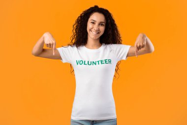 Neşeli gönüllü bayan parmaklarını kameraya doğru gösteriyor. Sarı Stüdyo Arkaplanının Üzerinde Duruyor. Bir şeylerin reklamını yapan aktivist. Şuraya bak, Gönüllü Reklam.