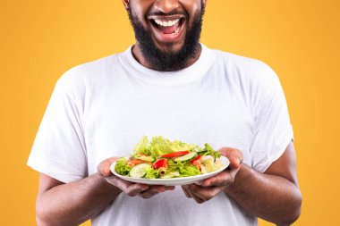 Sağlıklı yiyecekler. Heyecanlı Afrikalı Sebze Tutan Salata Tabağı Sarı Stüdyo Arkaplanının Üzerinde Duruyor. Erkek Diyet, Vejetaryen Yemek Tarifi ve Kilo Verme Konsepti