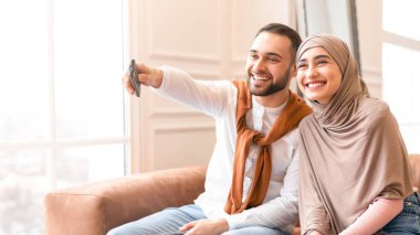 Mutlu, genç, Müslüman bir çift TV seyrediyor, evde birlikte oturuyor, hafta sonları dinleniyorlar. Arap Koca Kanalları Değiştiriyor Televizyon Uzaktan Kontrolü.