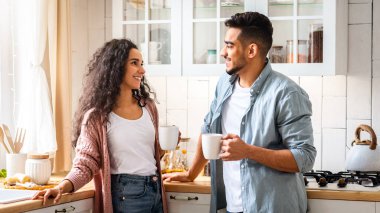 Mutlu bir Arap çiftin portresi, mutfak içinde kahve içip sohbet ederken, genç Orta Doğulu aşıklar evde sıcak içkinin keyfini çıkarırken, bardaklarını tutarken ve birbirlerine gülümserken,