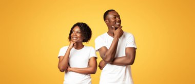 Düşünceli siyah erkek ve kadın yan yana durup düşünüyorlar, çenelerine dokunuyorlar ve gülümsüyorlar, kopyalama alanı. Genç Afro-Amerikan çift günü turuncu stüdyo arka planında birlikte hayal kuruyor.