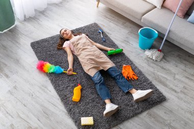 Bin yıllık kadının oturma odasında uyuması, temizlik malzemeleriyle çevrili, ev işlerinden yorgun, ev işlerinden yorgun, tam boy portre.