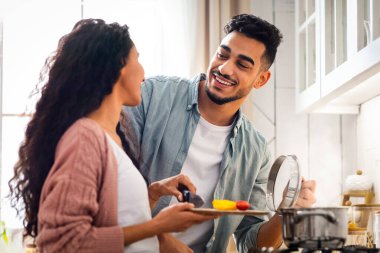 Mutlu Orta Doğulu eşler mutfakta birlikte yemek hazırlıyor, neşeli genç Arap aşıklar evde sağlıklı yemekler pişiriyor, fırında lezzetli sebze yemekleri yapıyor, yakın plan çekimleri yapıyor.