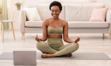 Çevrimiçi yoga. Lotus pozisyonunda oturup evde dizüstü bilgisayarda dinlenen mutlu siyah kadın meditasyonu. Meditasyon ve Rahatlama Konsepti. Seçici Odaklanma