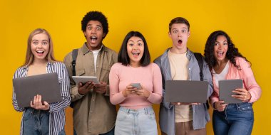 Dedikodu, şok edici haberler, online teknoloji ve takım çalışması. Şaşırmış genç öğrenciler dijital cihazlar kullanarak öğreniyor, turuncu arka planda izole edilmiş, fotokopi alanı, stüdyo çekimi