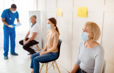 Klinikte kovid 19 aşısı için sırada bekleyen maskeli olgun kadın ve diğer hastalar doktorla iletişim kuruyor, koronavirüs karşıtı kampanyaya katılıyor, yer kopyalıyor.