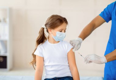 Siyah doktor, hastanede koruyucu maskeli küçük bir kıza koronavirüs aşısı yapıyor. Sağlık merkezinde covid-19 'a karşı bağışıklık kazanıyor. Küresel aşı kampanyası konsepti