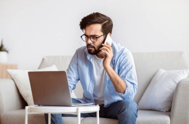 Mesafe işi. Doğulu serbest çalışan, telefonla konuşan ve evde dizüstü bilgisayar kullanan, bilgisayar üzerinde çalışan ve koltukta otururken cep telefonuyla projeyi tartışan milyoner bir Arap.