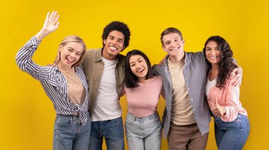 Üniversitede ya da yurt dışında eğitim. Neşeli genç çok ırklı uluslararası öğrenciler eğleniyor, gülüyor, sarılıyor ve turuncu arka planda izole edilmiş kameraya el sallıyorlar.