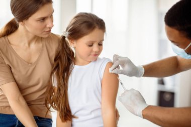 Doktor klinikteki küçük hastaya kovid 19 aşısı yapıyor. Annesiyle birlikte doktora giden sevimli bir kız. Coronavirus 'a karşı bağışıklık kazanıyor. İlaç, aşı ve sağlık hizmetleri kavramı