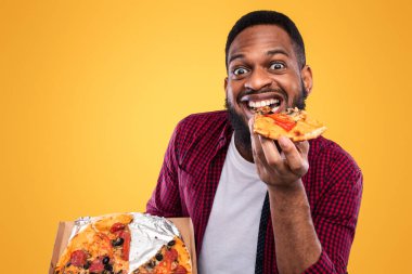 Stüdyoda aşırı yemek yeme pozuna gülümseyen pizza yiyen komik siyahi adamın portresi. Erkek Foodie Junk Food 'un tadını çıkarıyor. Sağlıksız Beslenme ve Aldatma Yemekleri