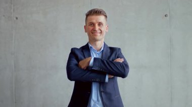 Takım elbise giymiş kendine güvenen bir profesyonel çağdaş bir ofiste beton bir duvara karşı duruyor. Işıklandırma modern estetiğe ve keskin giyim tarzına vurgu yapıyor..