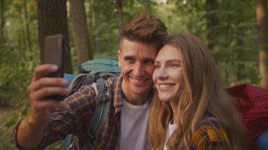 İki yürüyüşçü ormanda mutlu bir anı paylaşıyor, yeşil ağaçlar ve doğa arasında bir selfie ile maceralarını yakalıyorlar. Sırt çantaları bir gün açık havada keşif ve eğlencenin habercisi..