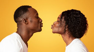 Portakal rengi stüdyo arka planında öpüşmek için birbirlerine çekilen zenci erkek ve kadının yan görünüşü, kopyalama alanı. Aşk, duygular, duygular. Afrikalı Amerikalı aşıklar sevgilerini gösteriyorlar.