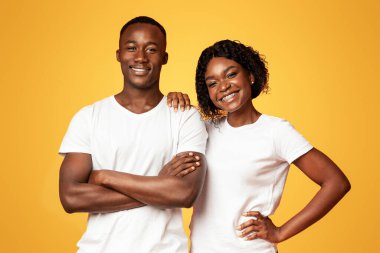 Gülümseyen siyah çift kot pantolon ve beyaz tişörtler içinde güzel bir erkek ve kadın turuncu stüdyo arka planında birlikte poz veriyorlar, güzel bayan kendine güvenen ve neşeli erkek arkadaşına dokunuyor, boş alan.