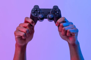 Siyah erkek eller video oyunları için mor arkaplan üzerinde joystick 'i tutuyor. Neon ışıklı, tanınmayan bir adam oyun, kırpılmış görüntü için modern teknolojilerden hoşlanıyor. Kopya alanı olan panorama.