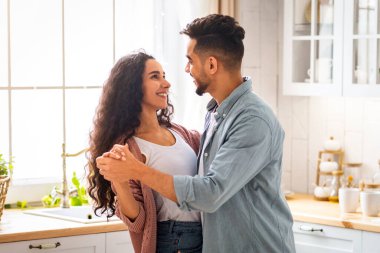 Mutfakta dans eden Arap eşleri, birbirine bakan ve gülümseyen Orta Doğulu romantik çift, evde eğlenen modern Müslüman çift, birlikte vakit geçirmenin tadını çıkarıyorlar, boşluğu kopyalıyorlar.