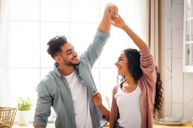 Romantik Arap eşler mutfakta dans ediyor, evde eğleniyor, modern Müslüman çift el ele tutuşuyor, gülümsüyor ve gülüyor, Orta Doğulu aşıklar birlikte vakit geçiriyorlar,