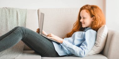 Dinleniyor ve dinleniyor. Yatak odasında ya da oturma odasında, dizüstü bilgisayar kullanarak, klavyede yazarak, internette sörf yaparak, sosyal medyada sohbet ederek gülümseyen kızıl saçlı genç kızın yan görüntüsü.