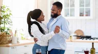 Romantik anlar. Genç mutlu siyah çift mutfakta dans ediyor, Afro-Amerikan aşıkları evde eğleniyor, lezzetli yemekler yiyor ve kırmızı şarap içiyor.