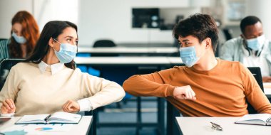 Virüs Kavramını yaymayı bırak. Birbirlerini selamlayan ve sınıfta dirsek tokuşturan koruyucu maskeler takan gülümseyen öğrenciler. Erkek ve kadın sıralarında oturuyor, lisede okuyor.