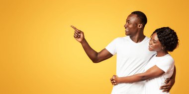 Birbirlerine sarılıp, fotokopi çeken, turuncu arka plan, panoramik fotoğraf çeken siyahi bir çift. Gülümseyen Afro-Amerikan bir kenara nişan alıp kadınına reklam ya da mesaj gösteriyor.