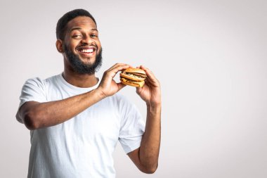 Elinde sağlıksız Burger pozu tutan gülümseyen siyah adam beyaz arka planda kameraya bakıyor. Erkek Beslenme ve Fast Food aşırı yeme alışkanlığı, Diyet Konseptinde Aldatma Yemeği. Stüdyo Çekimi