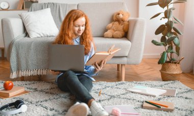 Sınava hazırlanıyorum. Zeki, güler yüzlü kız evdeki oturma odasında halının üzerinde oturuyor, kanepeye yaslanıyor, kağıt kitap tutuyor ve dizüstü bilgisayar kullanıyor, ödev yapıyor.