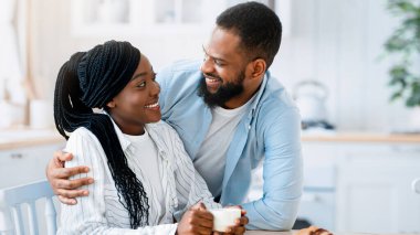 Mutlu genç siyah eşlerin sabah birlikte mutfakta vakit geçirmelerinin portresi, romantik Afrika kökenli Amerikalı çiftin evde kahvaltıda kruvasanlarla kahvenin tadını çıkarması,