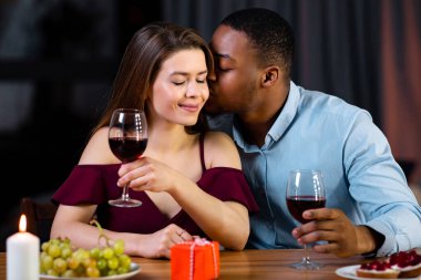 İki kişilik yemek. Romantik atmosferde evde yemek yiyen, şarap içen sevgililer gününü ya da yıldönümünü kutlayan siyahi erkek arkadaş sevgilisine aşk sözcükleri fısıldıyor.