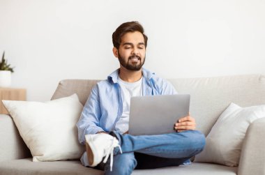 Yakışıklı Arap adam dizüstü bilgisayarla kanepede dinleniyor, film seyrediyor ya da internete takılıyor, milenyum doğusundaki çocuk oturma odasında bilgisayarla dinleniyor, boş zamanlarının keyfini çıkarıyor,