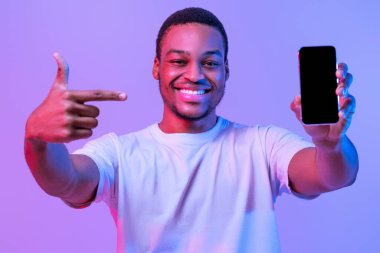 Mobil Teklif. Smartphone 'a boş ekranla işaret eden neşeli siyahi adam, uygulama veya web sitesi tasarımı için ekran kopyalama alanını gösterir, Mor Stüdyo Arkaplanının Üzerinde Neon Işıkta Durur, Mockup Image