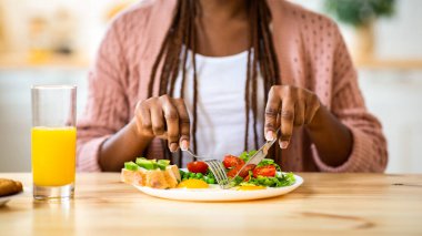 Gülümseyen Kara Kadın Mutfakta Lezzetli Kahvaltı Yapıyor, tanınmayan Afro-Amerikan Kadın Masada oturuyor ve Sağlıklı Lezzetli Yemeğin tadını çıkarıyor, Çatal ve Bıçak Kullanıyor, Kırpılmış Vuruyor
