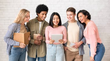 İlginç bir site, yeni çalışma uygulaması, test sonuçları online ve takım çalışması. Kitapları ve aletleri olan gülümseyen çok kültürlü genç insanlar sınıftaki Asyalı bayanların tabletlerine, stüdyo çekimlerine, boş alanlara bakıyorlar.