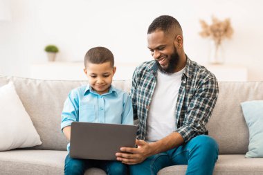 Afrikalı Amerikalı çocuk ve babası birlikte dizüstü bilgisayar kullanıyor, evdeki koltukta oturup bilgisayardan çizgi film izliyorlar. Genç Siyah Baba, oğluyla bağ kuruyor. İnterneti geziyor.