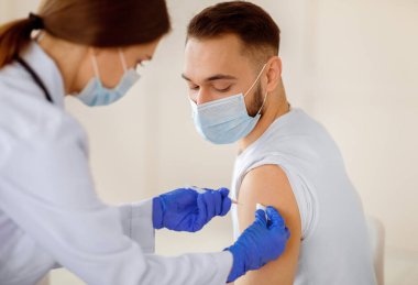 Kadın doktor, sağlık merkezinde maske takan genç hastaya koronavirüs aşısı yapıyor. Milenyum çocuğu covid-19 'a karşı aşı oluyor. Küresel bağışıklık kampanyası