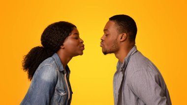 İlk öpücük. Romantik siyahi erkek ve kadının, sarı stüdyo arka planında öpüşmek için birbirlerine uzanması, genç Afrikalı Amerikalı aşıkların hassas anları, özgür bir boşluk...