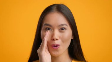 Uzun siyah saçlı genç bir Asyalı kadın elini şakacı bir şekilde ağzına atıyor, coşkuyla..