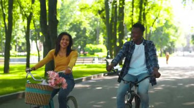 Genç bir Afrikalı Amerikalı çift yeşillik dolu güzel bir parkta bisiklet sürmekten hoşlanıyor. Neşeli bir günde doğa tarafından kuşatılmışken yan yana at sürerler, gülücüklerini ve gülüşlerini paylaşırlar..