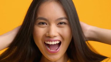 Neşeli bir Asyalı kadın, uzun saçlarıyla canlı sarı bir ortamda oynarken heyecanını ifade eder. Neşeli tavırları hayat dolu bir yaşam tarzını yansıtıyor, bin yıllık enerji ve pozitifliği yakalıyor..